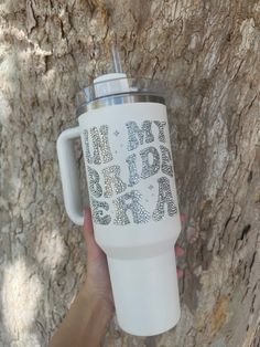 a person holding up a white coffee cup in front of a tree with words on it