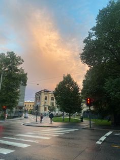 people are crossing the street in front of an old building and trees at sunset or dawn