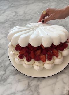 someone is decorating a cake with white frosting and strawberries on the top