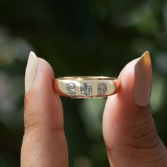 a woman's hand holding a gold ring with three diamonds