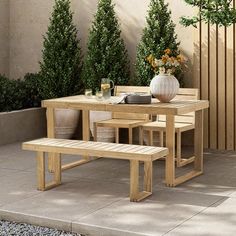 a wooden table and bench sitting next to each other on a stone patio with potted trees in the background