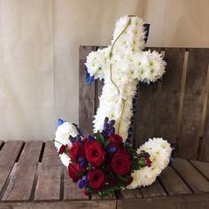 a bouquet of red, white and blue flowers in front of a cross on a wooden bench