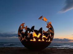 a sculpture on the beach with butterflies flying around it