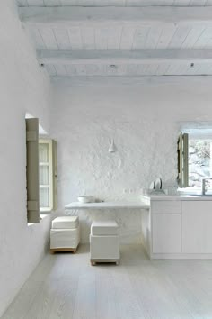 an all white bathroom with two sinks and stools in the middle of the room