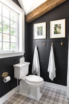 a white toilet sitting next to a window in a bathroom under two pictures on the wall