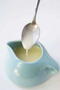 a spoon is pouring liquid into a small blue bowl on a white surface with a light green base