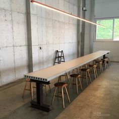 a long table with chairs and stools in an empty room next to a wall