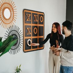 two people standing next to each other in front of a black and gold wall decoration