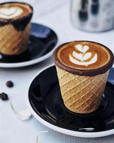 two ice cream cones with chocolate toppings on black plates next to coffee beans and silverware