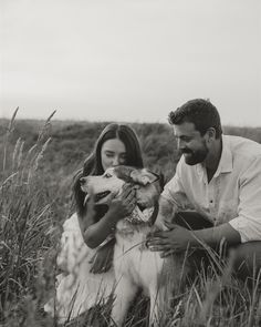 a man and woman petting a dog on the head in a field with tall grass