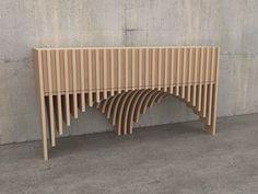 a wooden bench sitting next to a cement wall with curved wood slats on it