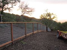 a fenced in area next to a dirt road with trees on the other side