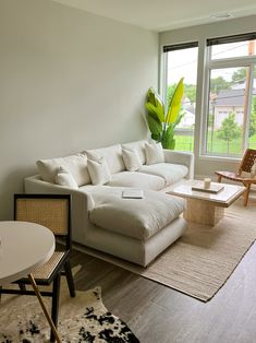 a living room filled with furniture next to a large window covered in green plants and greenery