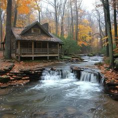 a log cabin in the woods next to a stream with water running through it and leaves on the ground