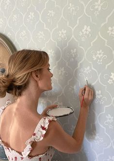 a woman in a white dress painting a wall with blue and white flowers on it