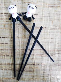 two panda bears sitting on top of black chopsticks