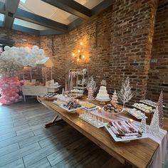 a table topped with lots of desserts next to a brick wall covered in balloons