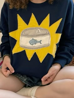 a woman sitting on the floor with her legs crossed and wearing a blue shirt with an image of a fish in it