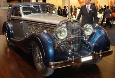 an antique car is on display in a building with people walking around it and two men standing next to it