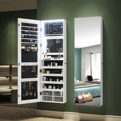 a white mirrored cabinet with jewelry hanging on it's sides in front of a green wall