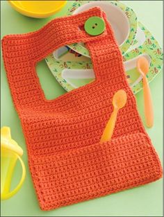 an orange crocheted bag with a green button on the side and spoons next to it