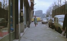 a woman walking down a sidewalk next to parked cars