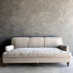 a white couch sitting in front of a wall with a cement background and wooden legs