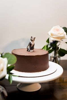 a small dog figurine on top of a chocolate cake with flowers in the background