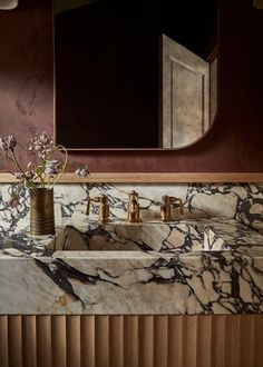 a marble sink with gold faucets and flowers in a vase on the counter