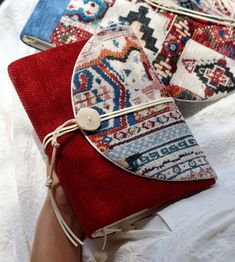 a woman's hand holding two red and blue purses on top of a white table