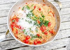 a bowl of spaghetti with tomatoes and parmesan cheese on the side sitting on a wooden table