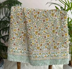 a green and yellow floral print blanket on a wooden stand next to a potted plant