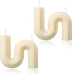 two white candles sitting next to each other on top of a white surface with one candle in the shape of a letter