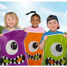 three children in halloween costumes holding up towels with monster faces on them and smiling at the camera