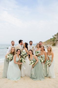 a group of people standing next to each other on top of a beach near the ocean