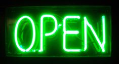 an open sign lit up in the dark with green neon lights on it's sides