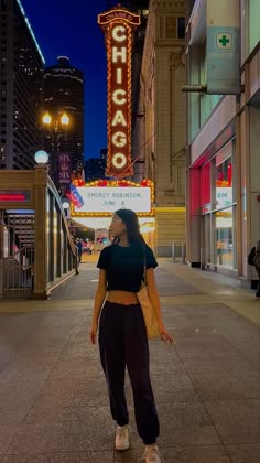 a woman standing on the sidewalk in front of a building with a sign that says chicago