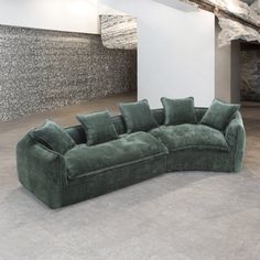 a large green couch sitting on top of a floor next to a stone wall and ceiling