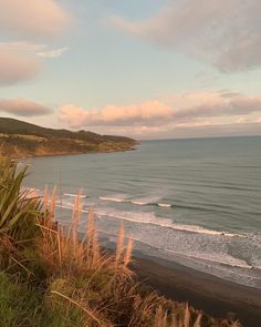 an ocean view from the top of a hill with grass growing on it and hills in the background