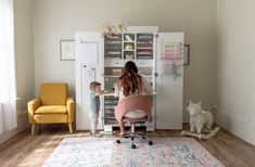 a woman and child are playing at the desk in their living room with yellow chairs