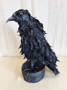 a black bird statue sitting on top of a piece of wood next to a white wall