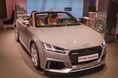 a silver convertible car on display at an auto show with two people in the back seat