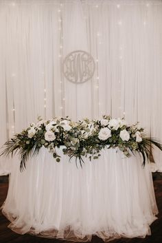 a table with white flowers and greenery on it in front of a curtained wall