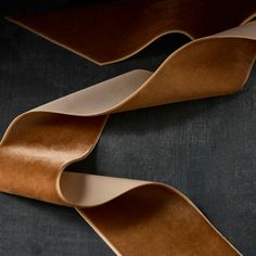 two pieces of brown leather on a black surface with one piece cut out and the other half rolled up