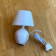 a small white lamp sitting on top of a wooden table next to a charger