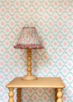 a small wooden table with a lamp on it in front of a floral wallpaper