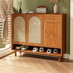 a wooden cabinet with two doors and shoes on it next to a window in a room