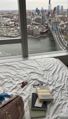 two books are sitting on top of a bed in front of a window overlooking the city