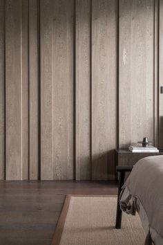 a bedroom with wood paneling on the walls and bed in the foreground, along with a rug on the floor