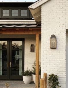 a white brick house with black glass doors and planters on the front porch area